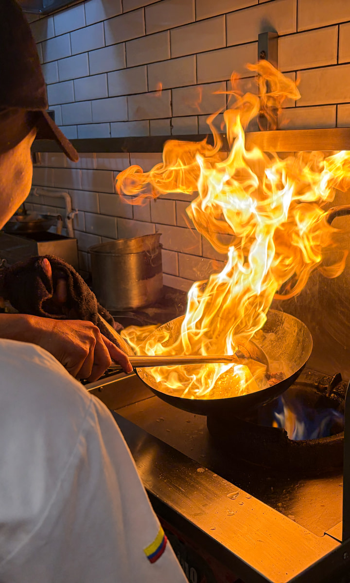 Cocinero de Renne trabajando frente a un wok mientras una llama alta ilumina la cocina
